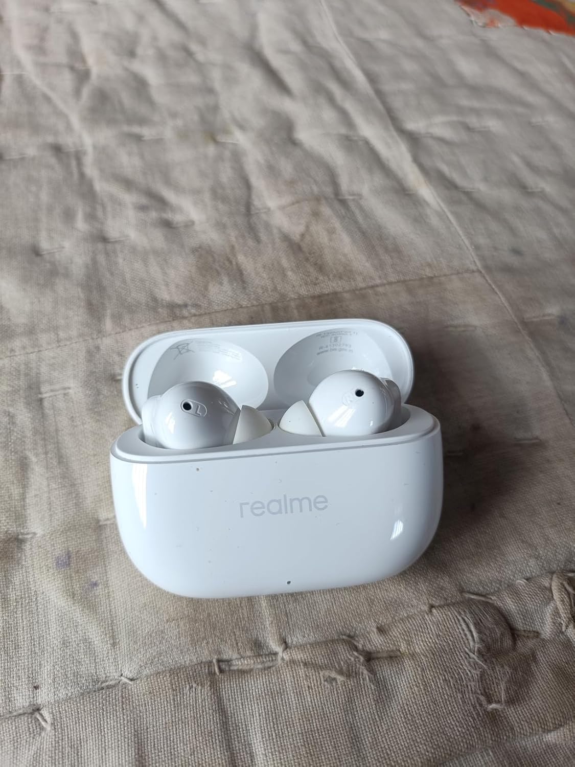 realme Buds T310 in Agile White, charging case open with both earbuds visible — verified-purchase customer photo showing the glossy premium finish