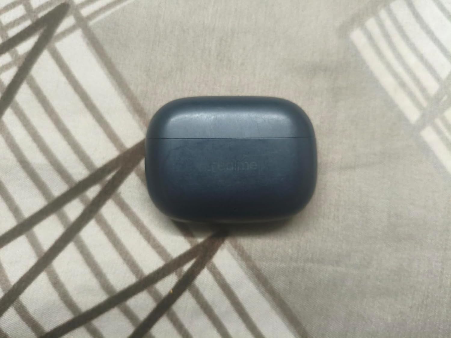realme Buds T310 charging case in hand for scale alongside the buds, highlighting the compact pebble-shaped form factor and USB-C charging port