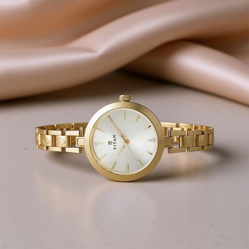 Titan Karishma NM2598YM01 lying on a beige surface showing the slim round gold case