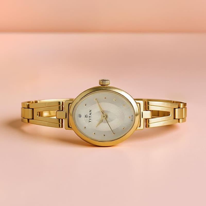 Titan Karishma Revive NM2594YM01 resting on a pink surface showing the bangle-style gold bracelet