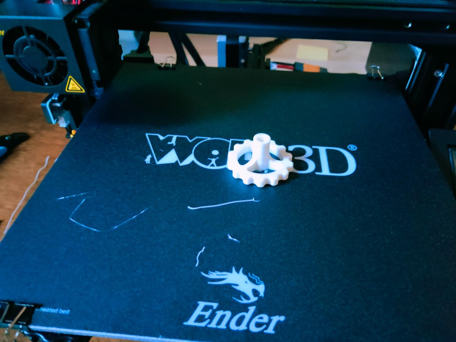 Ender 3 captured during a print run showing the V-slot Y-axis gantry, the aluminium sticker build plate and the Bowden tube feeding 1.75 mm PLA filament into the hot-end